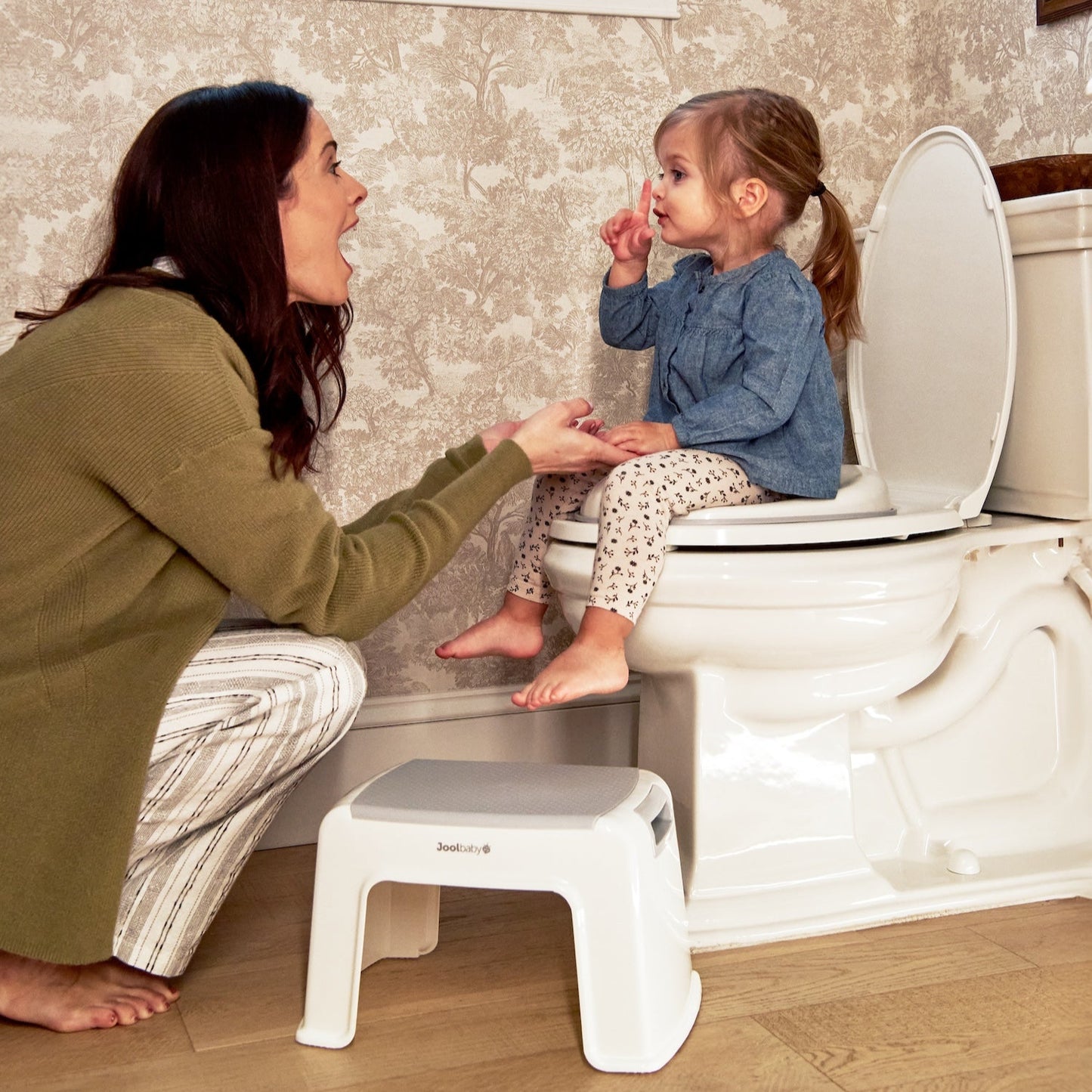 Woman teaching a child on a toilet with a step stool in a bathroom.