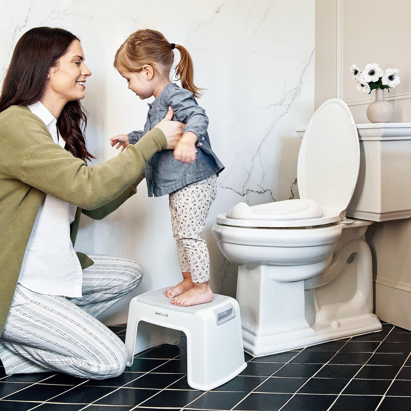 Woman helping a child on a step stool next to a toilet in a bathroom.