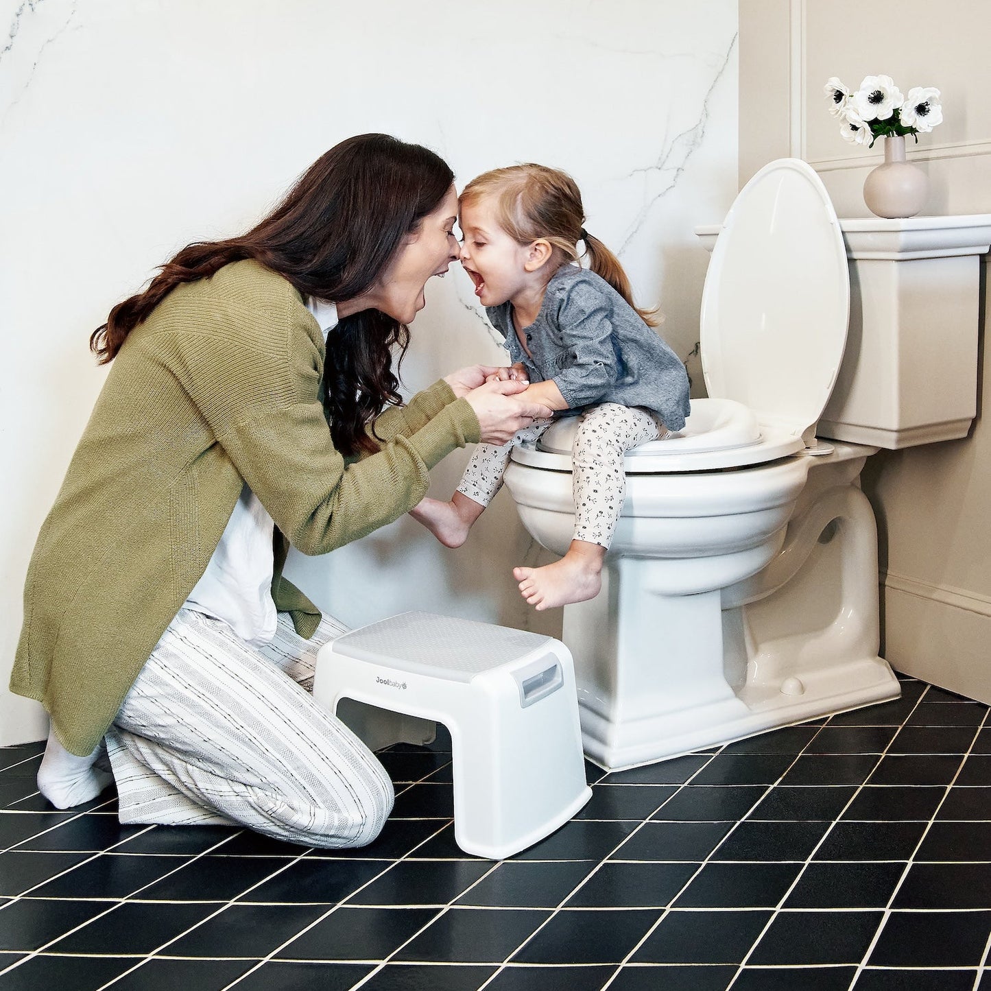 Woman teaching a child on a step stool next to a toilet in a bathroom.