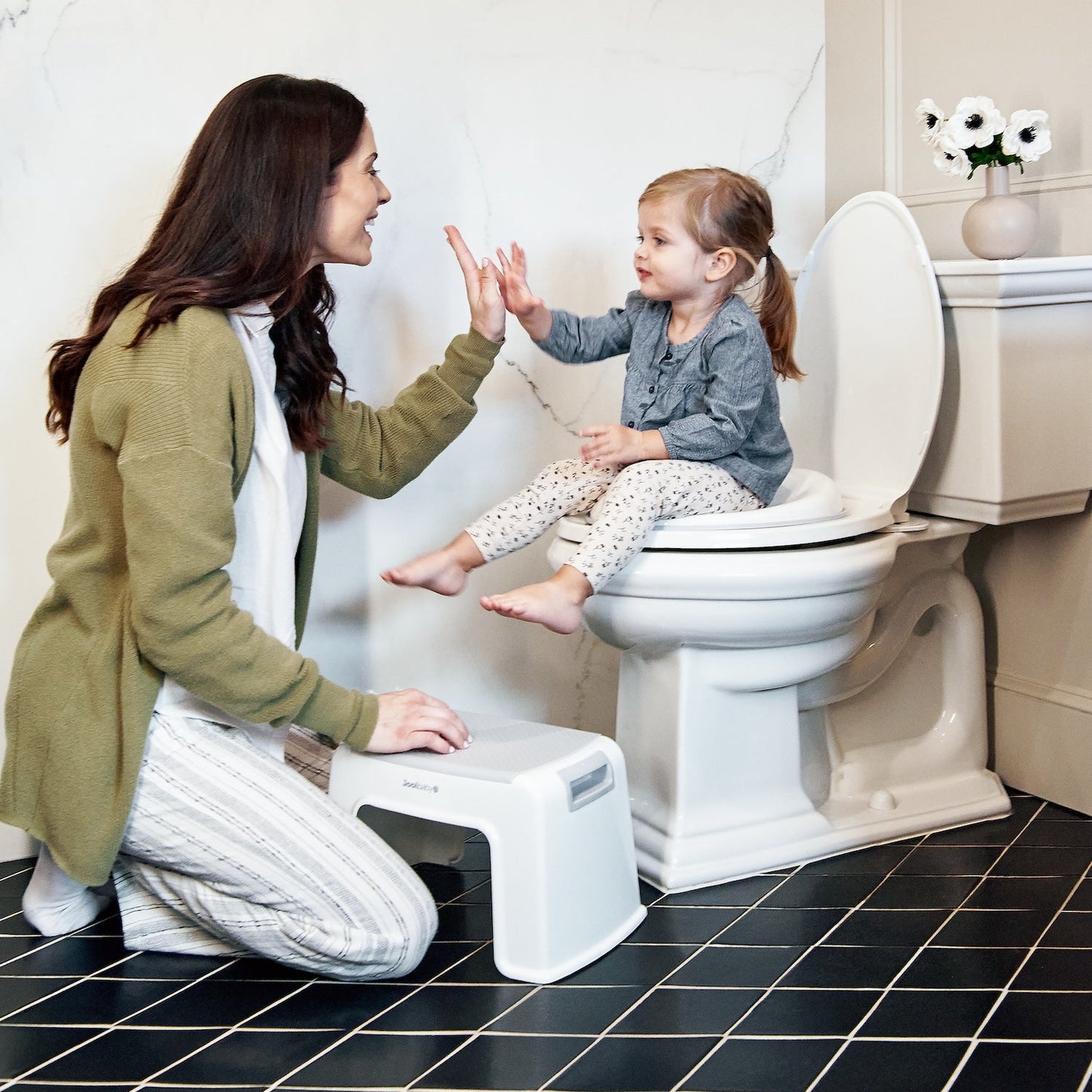 Woman teaching a child how to use a toilet with a step stool in a bathroom.
