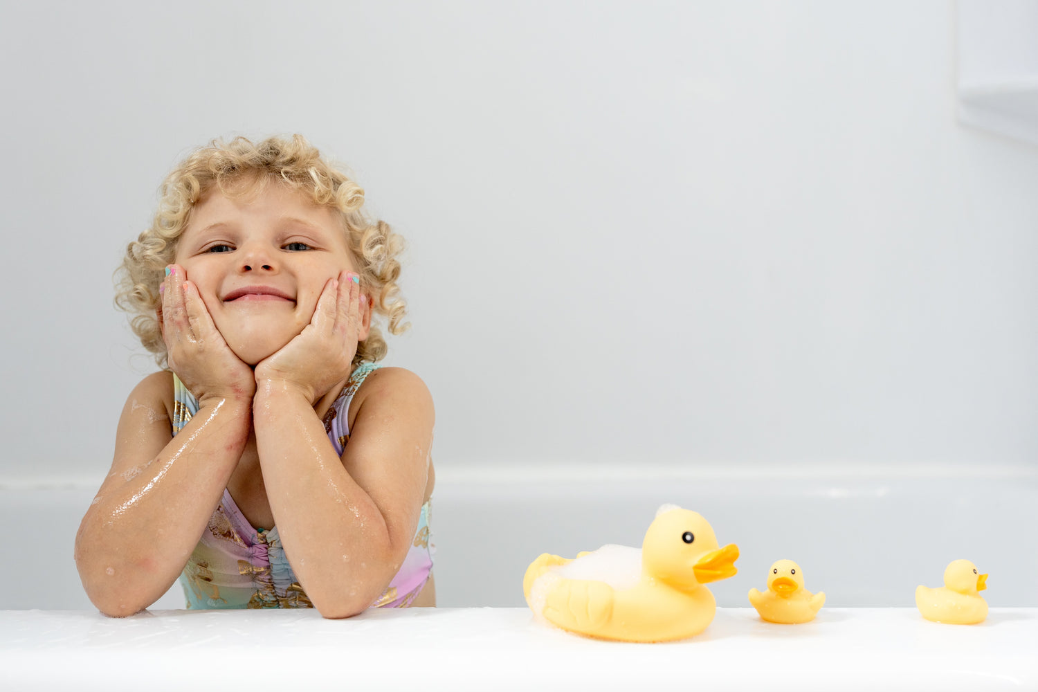 Child with wet hair and rubber duck toys on a white surface
