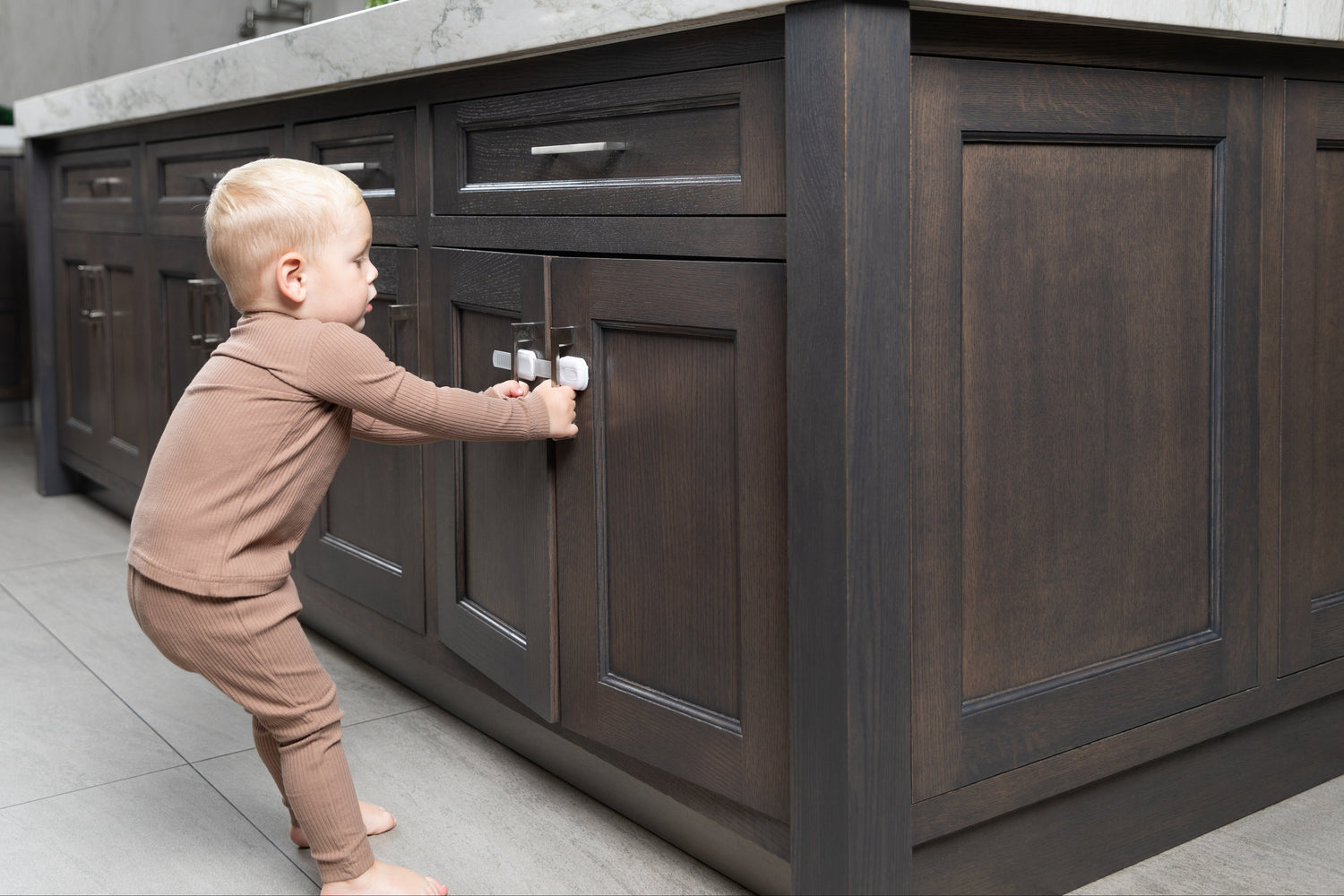 Child standing next to a kitchen island with dark wood cabinets and a light gray countertop trying to open doors
