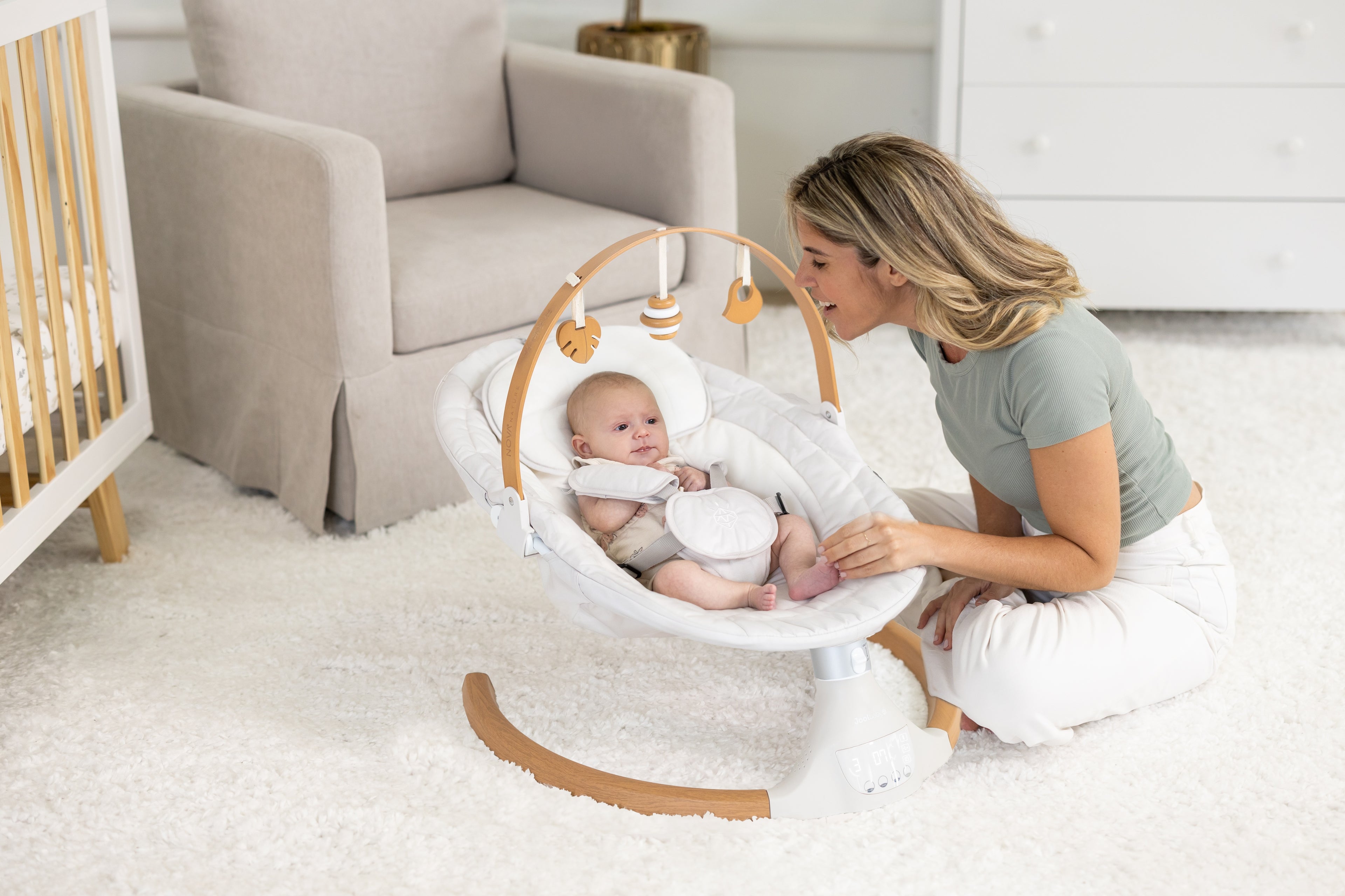 Woman holding a baby in a white and wooden baby swing in a nursery.