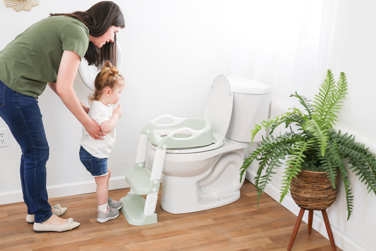 Woman helping a child use a toilet with a step stool in a bathroom.
