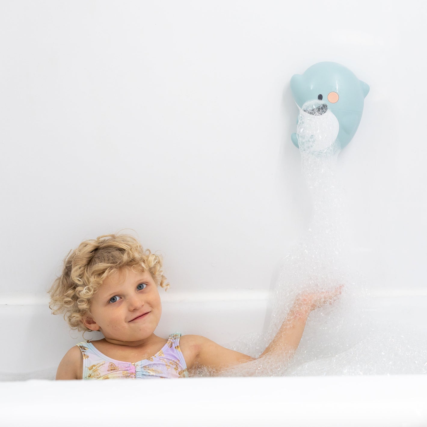 Child in a bathtub with bubble bath, holding a toy, in a bathroom setting.