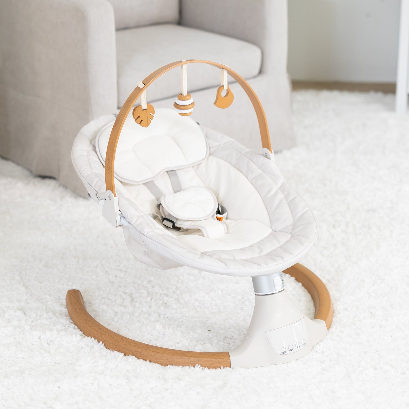 Baby swing in a nursery setting with a crib and chair in the background