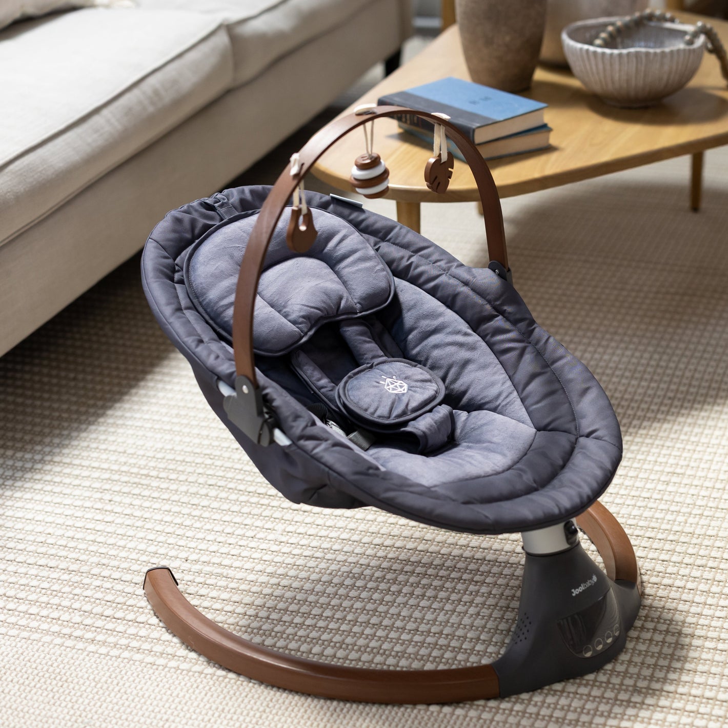 Baby swing in a living room setting with a sofa and coffee table in the background.