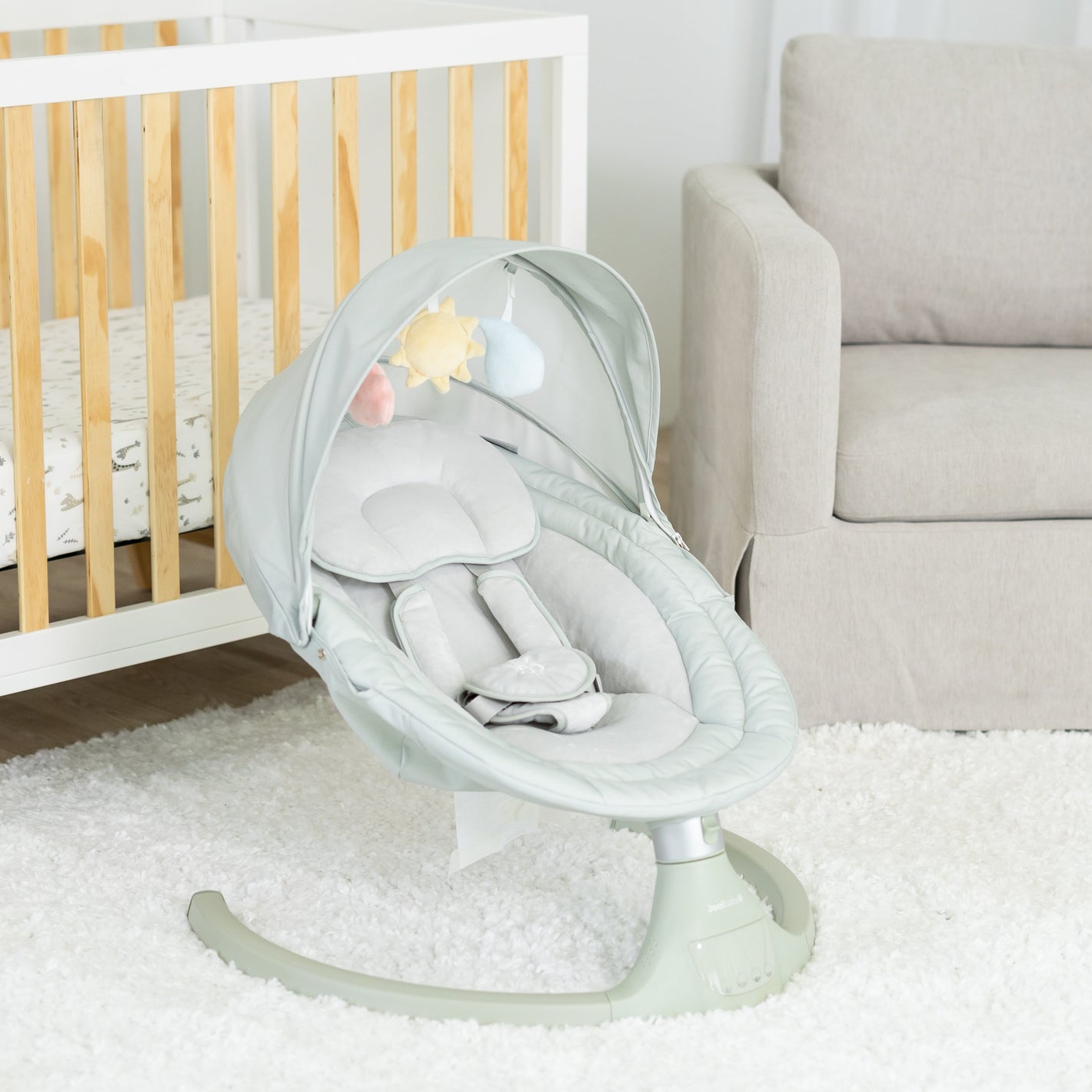 Baby swing in a nursery with crib and chair in the background