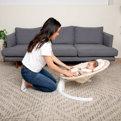 Woman adjusting a baby in a white baby swing in a living room.