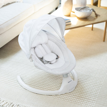White baby swing in a living room setting with a couch and coffee table.