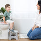 Child using a step stool on a toilet with a woman beside them in a bathroom setting.