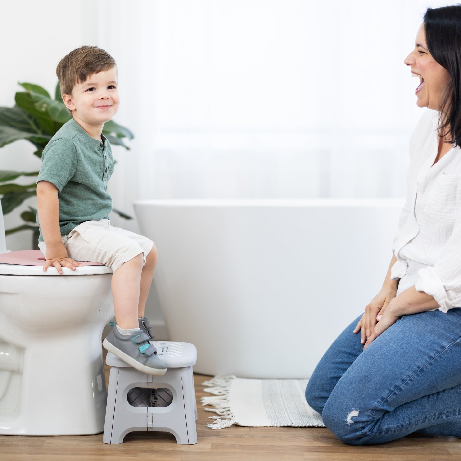 Child using a step stool on a toilet with a woman beside them in a bathroom setting.