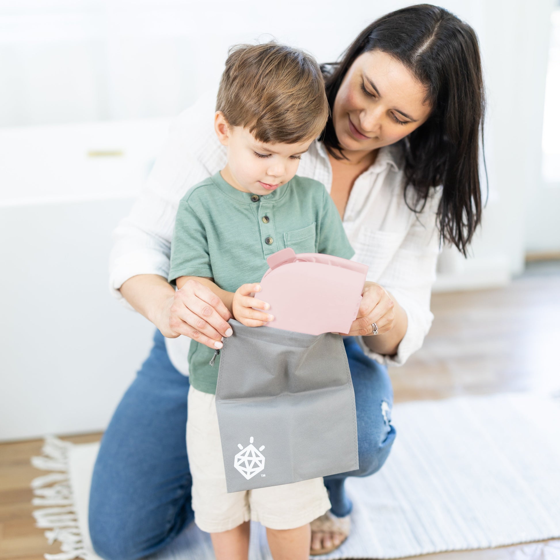 Woman and child holding a gray bag with a logo on a wooden floor.