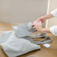 Person opening a gray bag with a white logo on a wooden surface