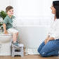 Child using a step stool on a toilet with a woman beside them in a bathroom setting.