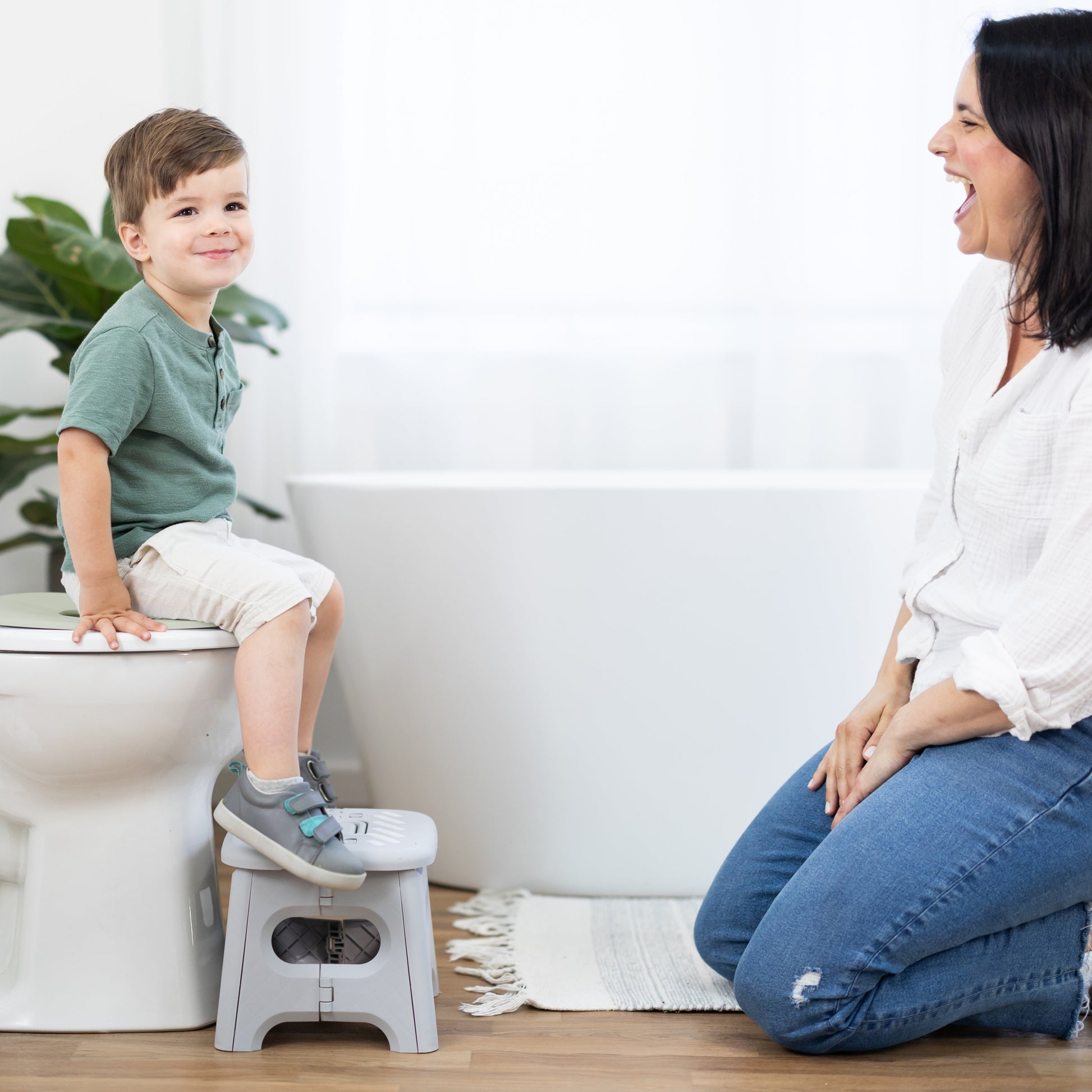 Child using a step stool on a toilet with a woman beside them in a bathroom setting.