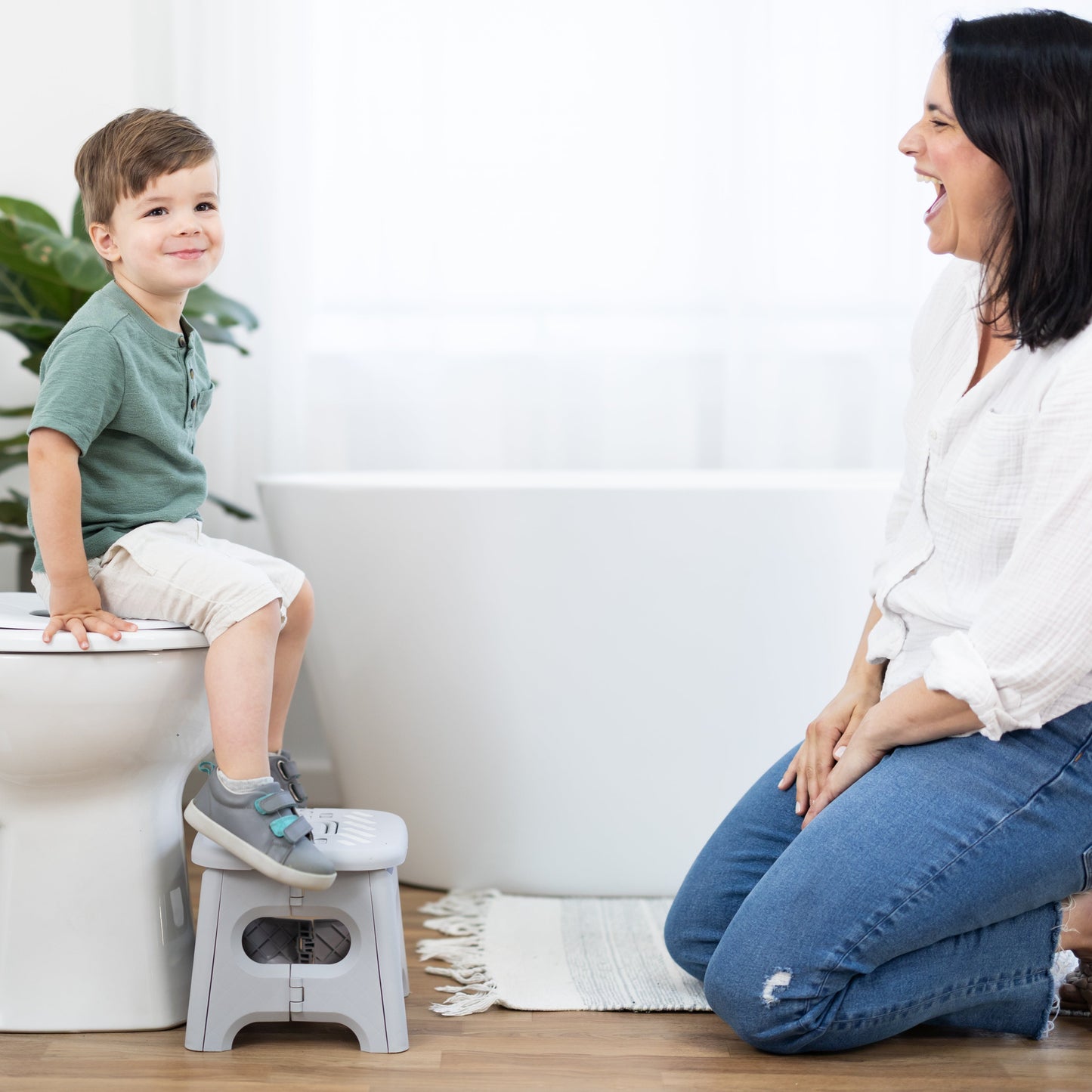 Child using a step stool on a toilet with a woman beside them in a bathroom setting.