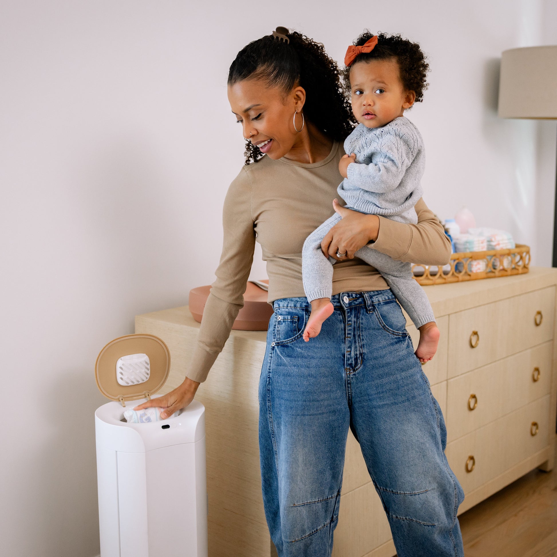 Woman holding a baby next to a diaper changing station in a nursery.
